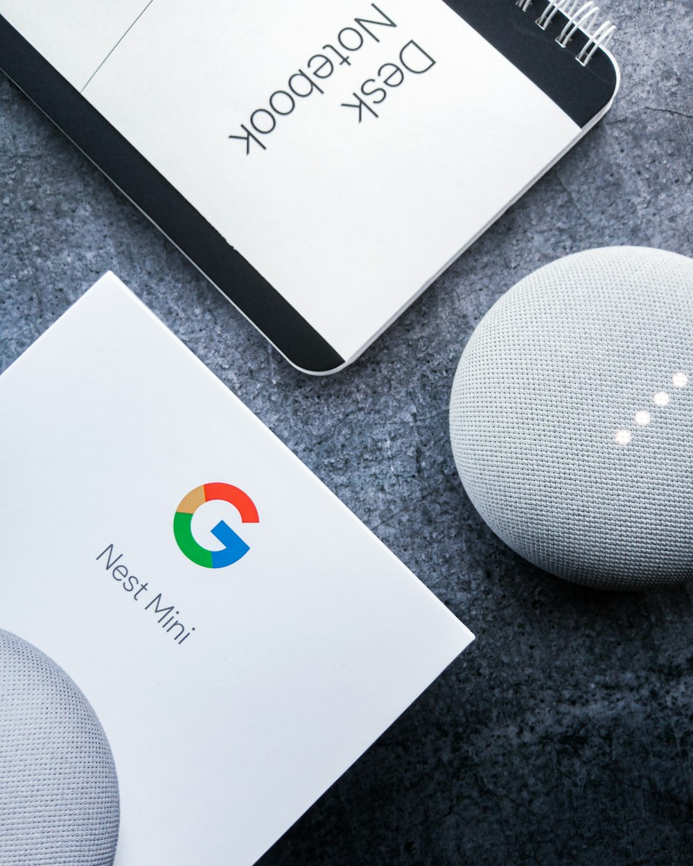 Flatlay photography of the google home mini along with a minimalistic notebook to boost productivity.